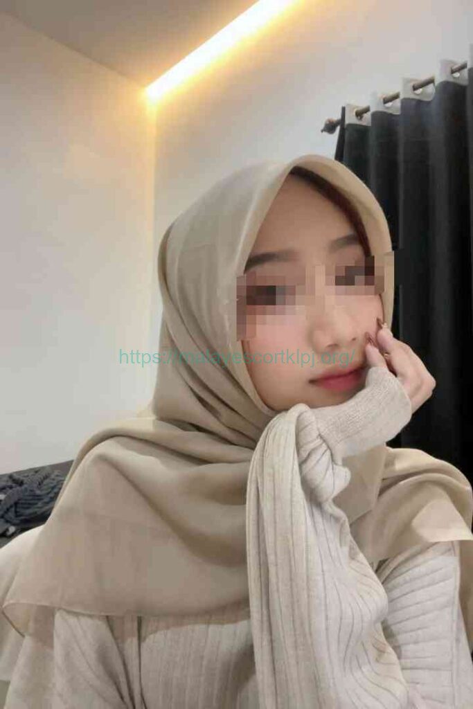 Young woman wearing a beige hijab, resting her chin on her hand.